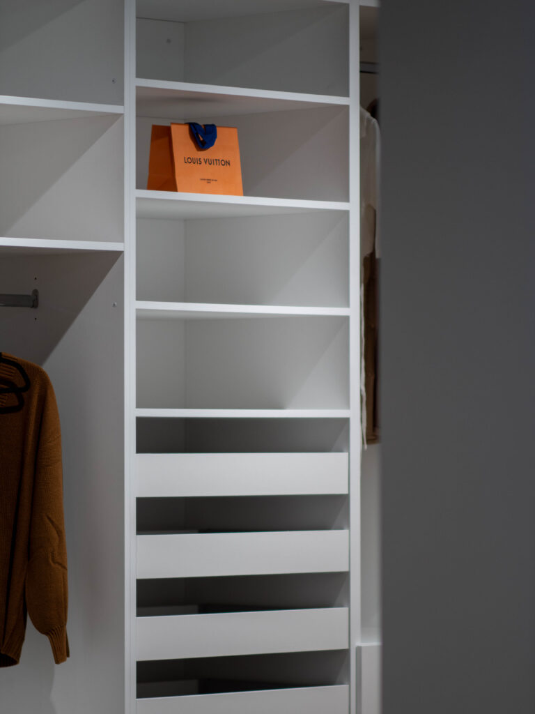 Custom white built-in closet shelving with open cubbies and drawers, featuring clean modern finish carpentry and hanging storage area