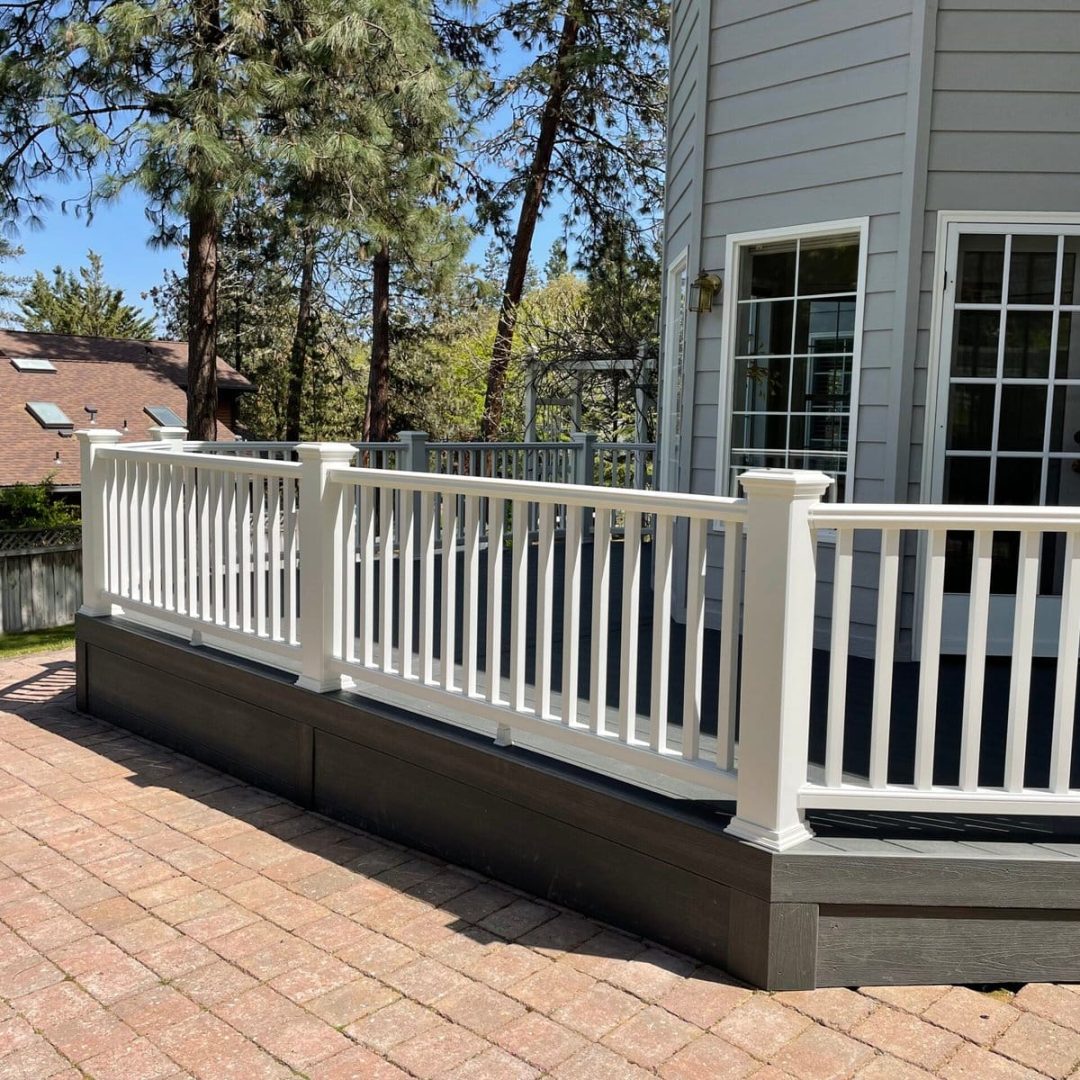 Composite deck with white railing beside a gray home